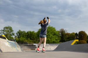 Jeune femme fait un spin en patins au milieu d'un skatepark en portant un t-shirt copains roulettes